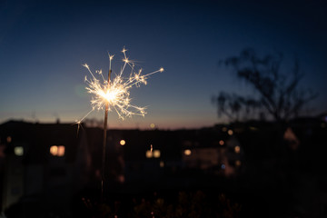 The beginning of a burning sparkler above the roofs of a small town at dusk; blurred background