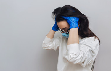 Young nurse doctor in a protective blue medical mask and glasses holds his head in his...