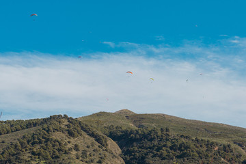 Fototapeta na wymiar Parapentes volando sobre cielo azul con nubes y sobre una montaña.