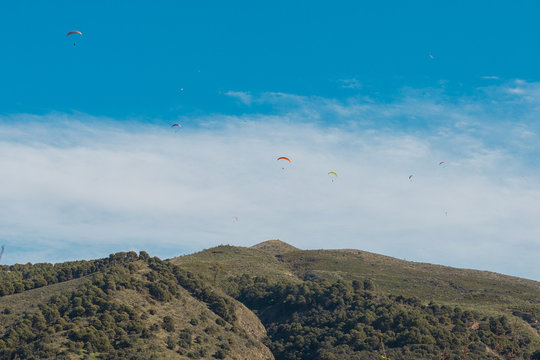 Parapentes volando sobre cielo azul con nubes y sobre una monta&ntilde;a.