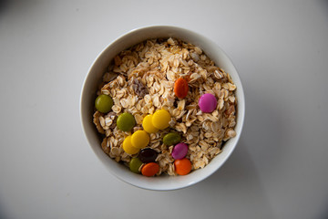 a bowl of corn flakes and colourful bonbons on white background

