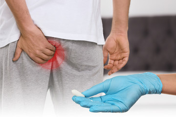 Doctor holding suppository for hemorrhoid treatment and man suffering from pain, closeup