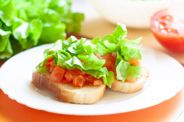 Bruchetta with tomatoes and lettuce on a white plate, vegetables and white bowl in the background