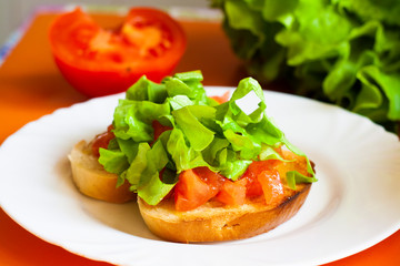 Sandwich with tomatoes and lettuce on a white plate, vegetables in the background