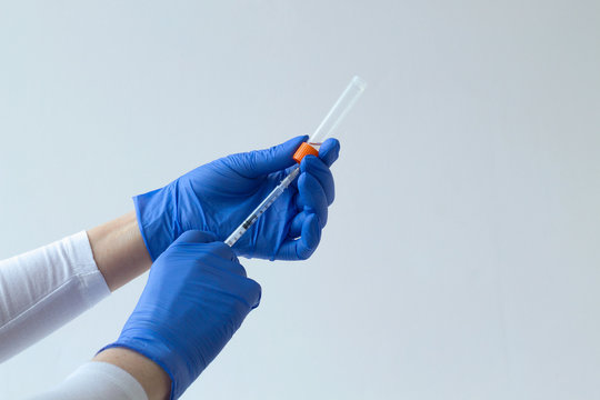 Gloved Hand Holding A Syringe On Grey Background. Medical Healthcare. Doctor Hands In Gloves Prepares A Vaccine In An Injection Syringe. People In White Uniform In Lab. Copy Space