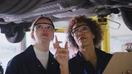 Female tutor and student looking underneath car on hydraulic ramp on auto mechanic course - shot in slow motion 