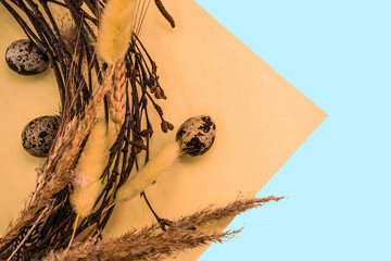 Happy Easter Holiday flat lay decoration with quail eggs and wreath from the brunches,ears and quail feathers on the combined blue and yellow background.Copyspace for mock-up