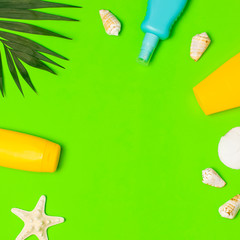 Sun protection Summer background vacation travel concept Yellow blue bottles of sunscreen cream tropical palm leaves shells starfish on green background top view flat lay copy space. Summer cosmetics