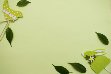 Easter frame made of light green felt figures of a bird and rabbit,leafs of ficus on the green background. Copyspace for greeting text.Flat lay Happy Easter