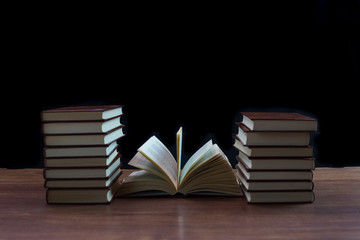 Libros antiguos apilados sobre mesa de madera con fondo oscuro.