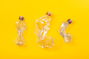 Three used plastic bottles on yellow background. The concept of pollution of the planet and the oceans with plastic waste, instructions on how to crush a bottle.