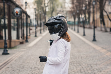 a thin girl in a white medical coat and overalls holds a syringe. A woman in a motorcycle helmet with a medical mask. coronavirus, disease, infection, quarantine, covid-19