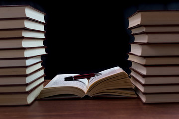 Libros antiguos apilados sobre mesa de madera con fondo oscuro.