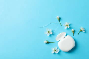 Dental floss and flowers on blue background, space for text