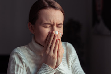 Cough in tissue covering nose and mouth when coughing. European woman sick with flu at home.