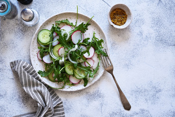 Vegetable salad with arugula radishes and cucumber on a concrete background