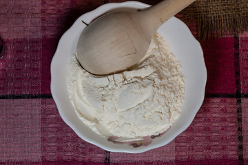 In a bowl is flour. On top is a wooden spoon.