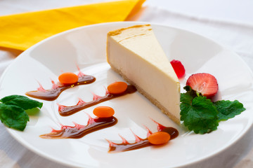New Yorker cheesecake on a white decorated plate with mint leaves and strawberries