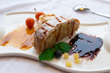 Apple strudel with ice cream on a decorated white plate with mint leaves and cherries