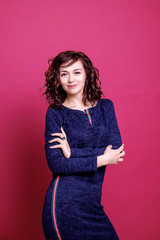 Sexy curly brunette girl is standing in a blue dress on a red background. Manager photo session.