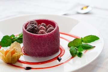 Raspberry tartlet on a white plate with mint leaves and physalis