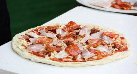 Italian cuisine. Preparation pizza. Dough, ketchup, bacon, salami, sausage and cheese on a white board on a wooden table. Background image, copy space