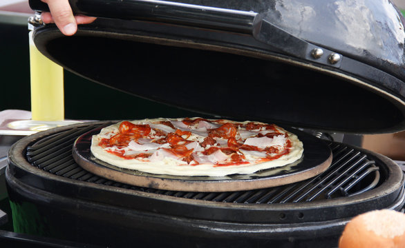 Italian cuisine. Preparation pizza on grill with hand. Dough, ketchup, bacon, salami, sausage and cheese on a white board on a wooden table. Background image, copy space