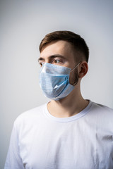 A young man in a medical mask on a white background looks away. Self isolation