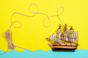 Toy ship is floating on the blue paper-cut waves, rope is twisted by loops above a ship on the...