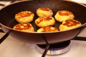Cheesecakes are cooked in a black pan on natural gas on the stove