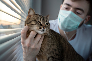 The man is a veterinarian in a mask holding a striped brown cat. Medical examination