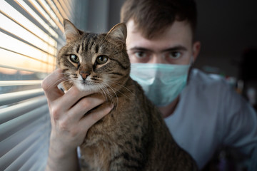 A male veterinarian in a medical mask holds a striped brown cat.
