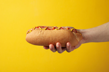 Hand holds tasty hot dog on yellow background