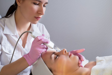 close-up, professional beautician using an ultrasonic facial cleanser, cleans the skin of a girl patient, in a beauty salon