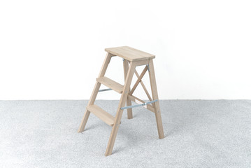 Wooden staircase and stool. A room in the photo studio. White wall. Grey floor. Copy space. Place for text and design.