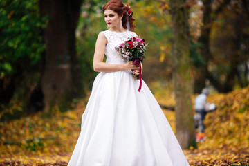 Fototapeta na wymiar Young bride in wedding dress walking in a park. White luxury gown fashion for woman. The bride walks in the park.