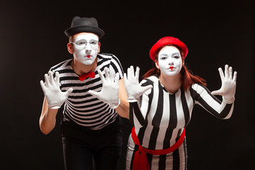 Portrait of man and woman mime artists performing, isolated on black background. Mimes in striped...