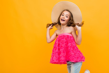 young tourist girl in a summer pink t-shirt with a straw hat on her head on a yellow studio background
