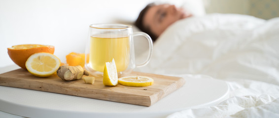 Cup with antipyretic drugs for colds,flu.Sick man in bed. Tea with citrus vitamin C,ginger root,lemon,orange.Wooden tray. Home self-treatment.Medical quarantine antiviral covid-19 coronavirus therapy