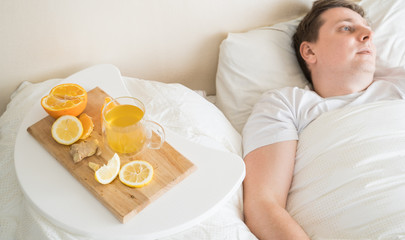 Obraz na płótnie Canvas Cup with antipyretic drugs for colds,flu.Sick man in bed. Tea with citrus vitamin C,ginger root,lemon,orange.Wooden tray. Home self-treatment.Medical quarantine antiviral covid-19 coronavirus therapy