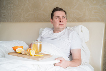 Cup with antipyretic drugs for colds,flu.Sick man in bed. Tea with citrus vitamin C,ginger root,lemon,orange.Wooden tray. Home self-treatment.Medical quarantine antiviral covid-19 coronavirus therapy