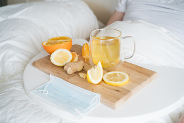 Cup with antipyretic drugs for colds,flu.Sick man in bed. Tea with citrus vitamin C,ginger root,lemon,orange.Wooden tray. Home self-treatment.Medical quarantine antiviral covid-19 coronavirus therapy