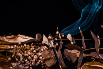 Stick holder and incense stick with leaves and flowers on black background