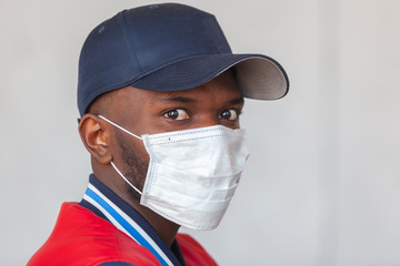 Close up photo of handsome african man in a cap and casual clothes wearing medical mask shocked with coronavirus 2019 danger