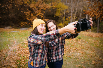 two friends taking a selfie with a camera in a park in autumn