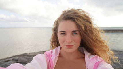 selfie of young beautiful blonde girl shake hair in the wind against a blue sky with clouds in...