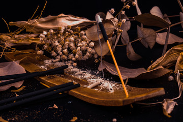 Stick holder and incense stick with leaves and flowers on black background