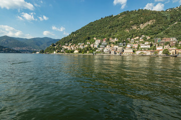 Como, ITALY - August 4, 2019: Apartments, villas, hotels on the green forested mountainsides near Lake Como. Beautiful Italian Como city. Warm sunny summer day in very popular holiday destination