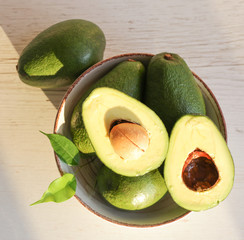 Whole and halved avacado on a light wooden background