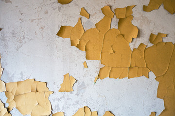 Old plastered wall with partially peeling and cracked yellow paint.